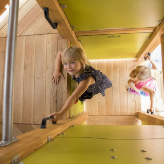Klettern für Kinder – Zwei Mädchen klettern in das Innere eines grüngelben Spielturms.