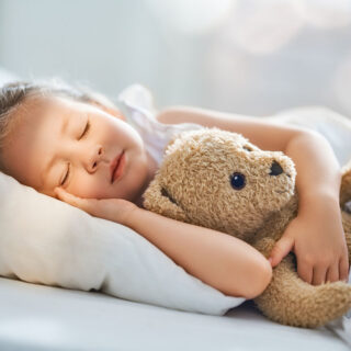 Schlafbedarf Ihrer Kinder – ein Kind schläft mit Teddy im Arm.