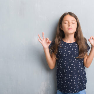 Meditation für Kinder – ein Mädchen mit geschlossenen Augen hebt die Hände zur Meditationsgeste.