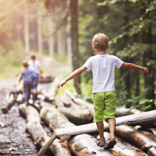 Gleichgewichtsübungen für Kinder – Jungen balancieren im Wald einige Baumstämme entlang.