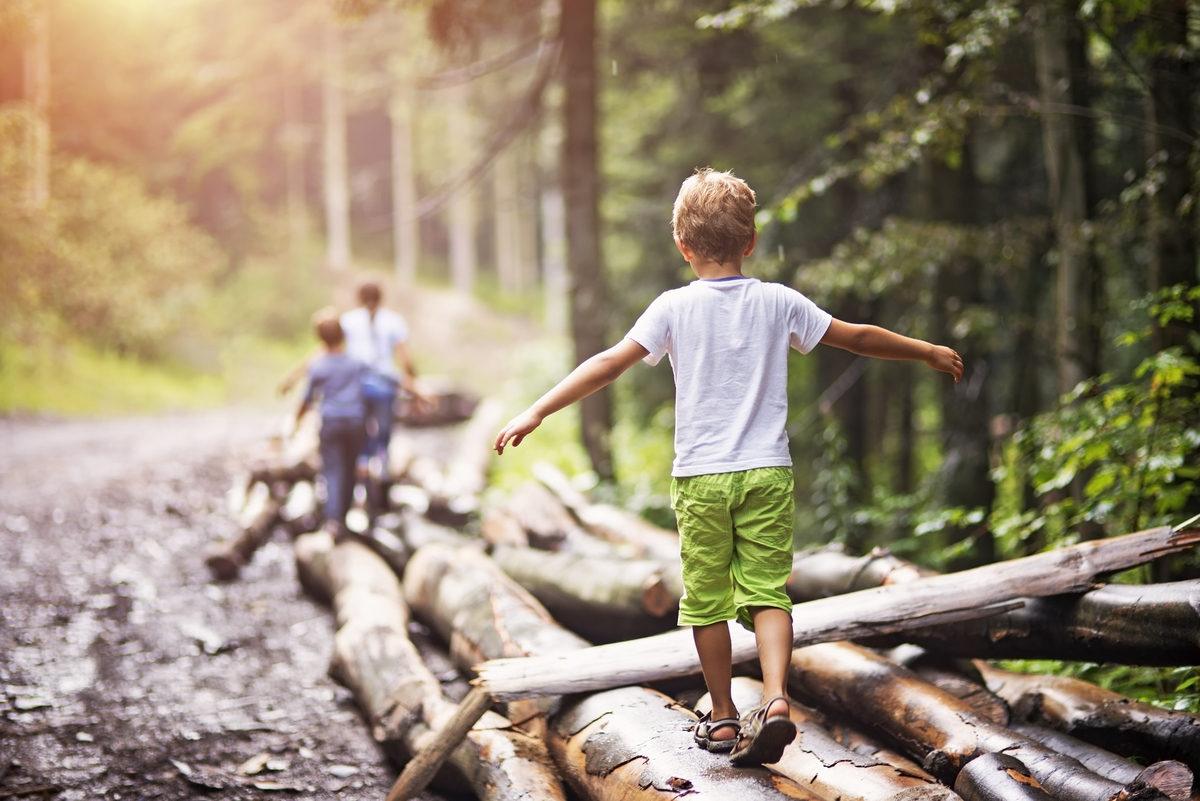 Gleichgewichtsübungen für Kinder – Jungen balancieren im Wald einige Baumstämme entlang.