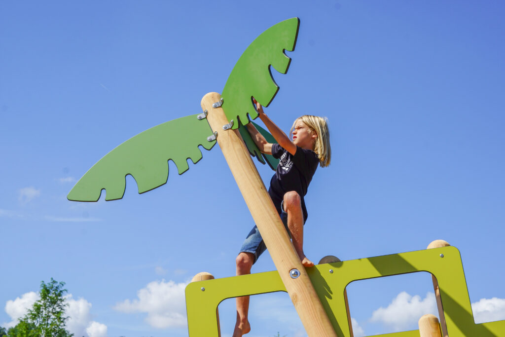 Themenspielplatz – ein blonder Junge klettert auf die Palme der Spielanlage Geländewagen.