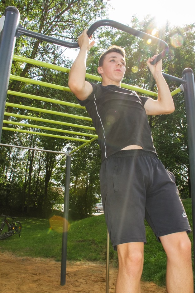 Calisthenics-Übungen: ein junger Mann macht Klimmzüge an einer Calisthenics-Anlage.