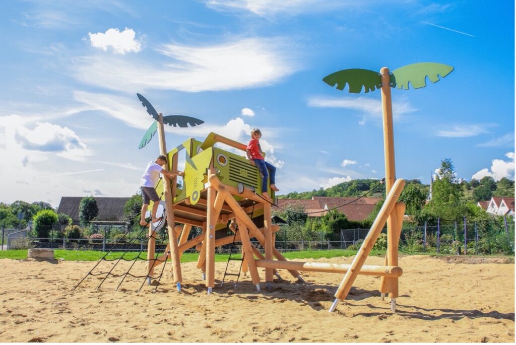 Die Spielanlage in Form eines Geländewagens mit Kletterelementen und palmenförmigen Pfosten ist eine prima Grundlage für einen Themenspielplatz im Dschungel-Design.