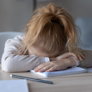 Zeit-, Erwartungs- und Leistungsdruck lösen Stress bei Kindern aus – ein Mädchen liegt mit dem Kopf auf einer Tischplatte.