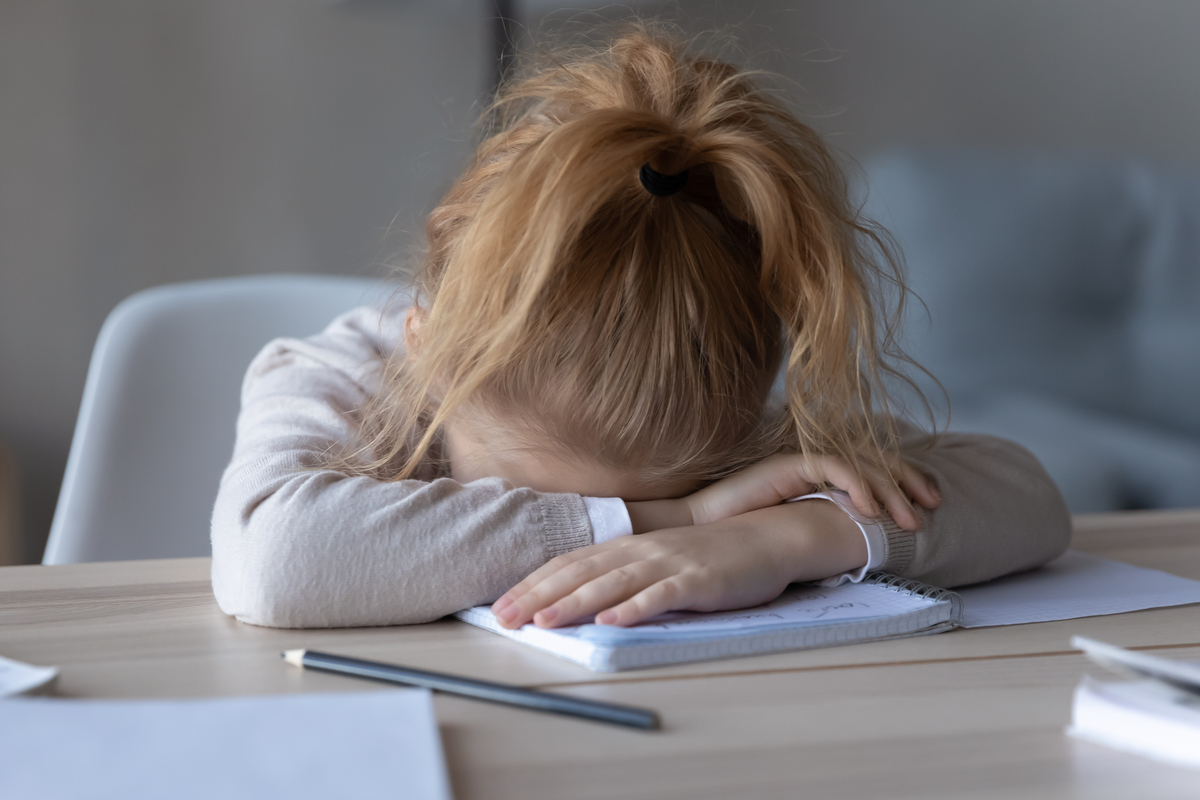 Zeit-, Erwartungs- und Leistungsdruck lösen Stress bei Kindern aus – ein Mädchen liegt mit dem Kopf auf einer Tischplatte.
