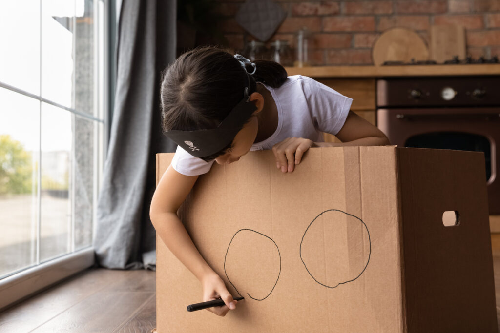 Kreativität bei Kindern fördern – Ein Mädchen mit Piratenhut bemalt einen Karton als Schiff.