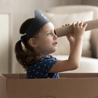 Kreativität bei Kindern fördern – Ein Mädchen mit Piratenhut benutzt eine Papprolle als Fernrohr.