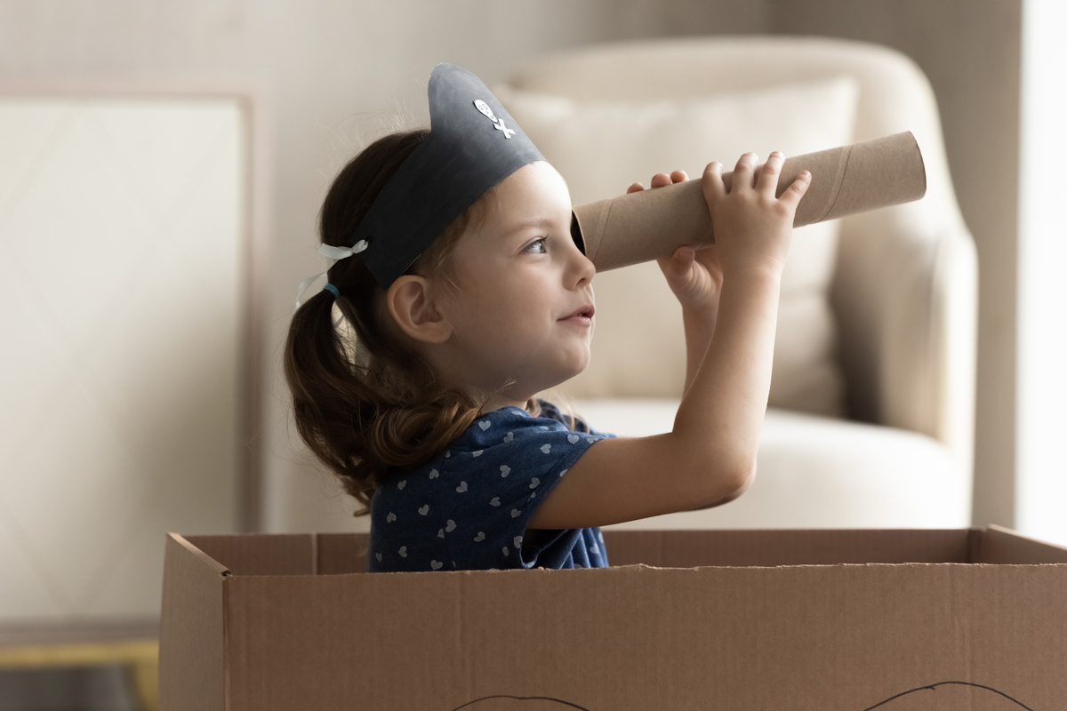 Kreativität bei Kindern fördern – Ein Mädchen mit Piratenhut benutzt eine Papprolle als Fernrohr.