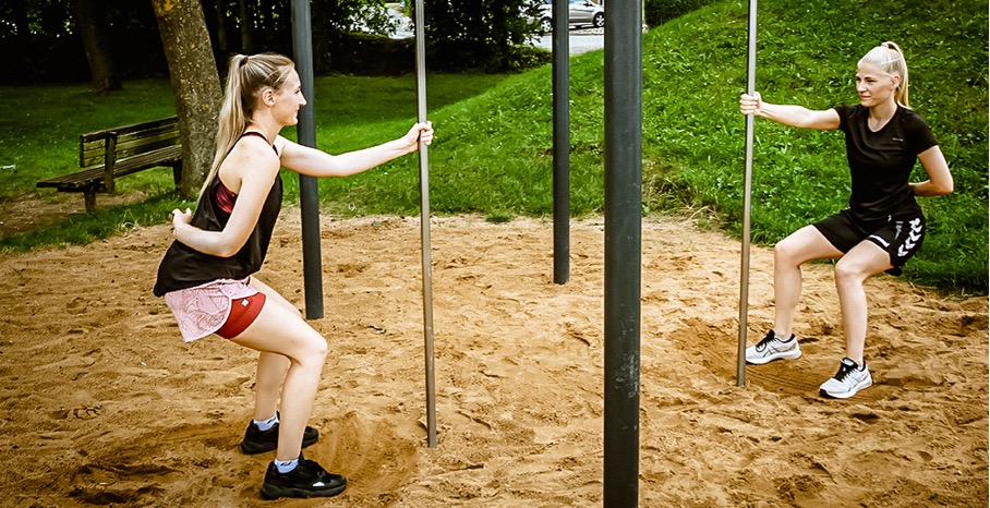 Outdoor Fitness – Zwei Frauen machen Squats an der Stange eienr Calisthenics Anlage.
