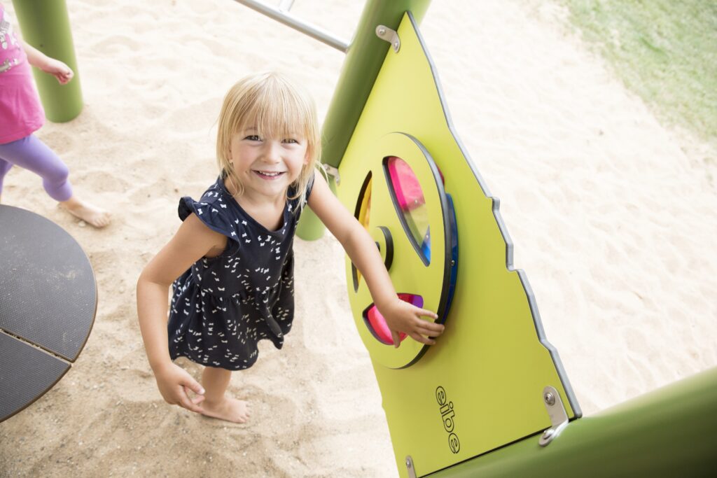Farbwahrnehmung bei Kindern – Ein blondes Mädchen steht vor der Farbtafel an einer Spielanlage von eibe.