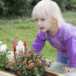 Gärtnern für Kinder – Ein blondes Mädchen stützt sich an eine, Pflanzkübel ab.