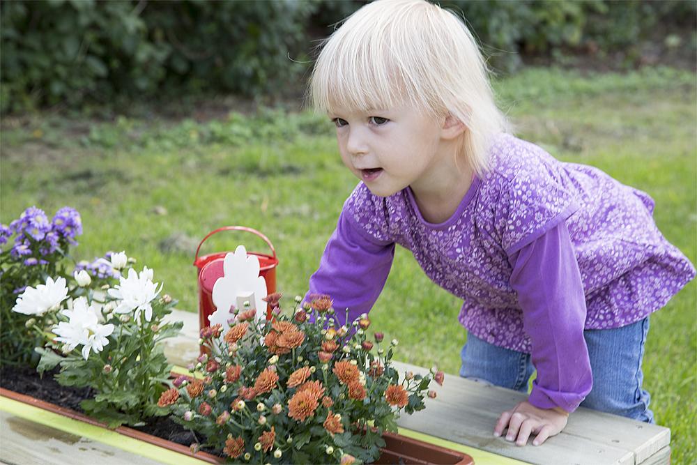 Gärtnern für Kinder – Ein blondes Mädchen stützt sich an eine, Pflanzkübel ab.