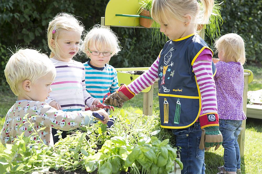 Gärtnern für Kinder – Kinder stehen um Pflanzkübel herum, die mit Kräutern bepflanzt sind.