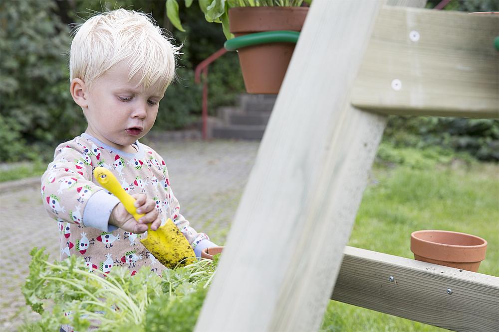 Gärtnern für Kinder – Ein kleiner Junge sitzt im Gras und hält eine Gartenschaufel in der Hand.