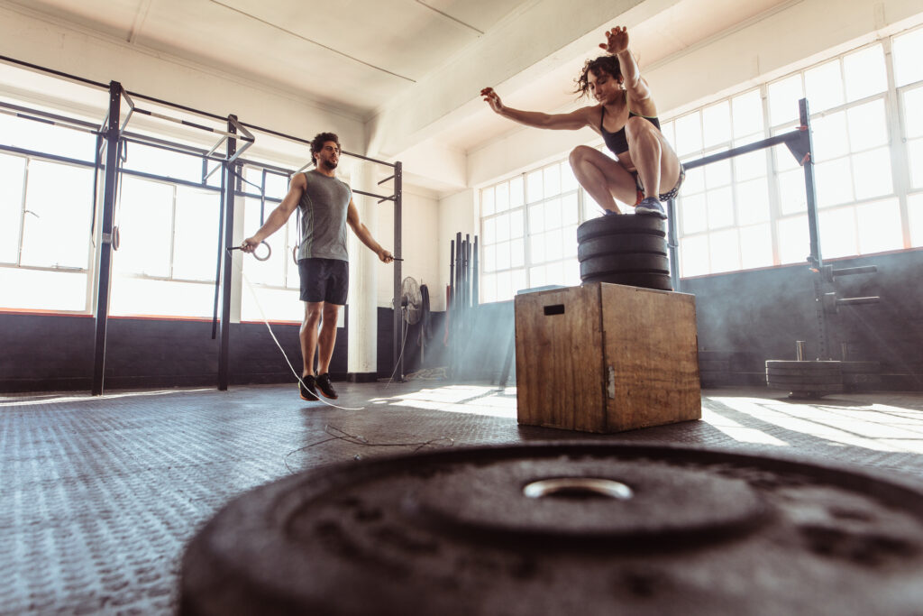 Ein Sportler und eine Sportlerin führen Zirkeltraining Übungen im Fitnessstudio durch.