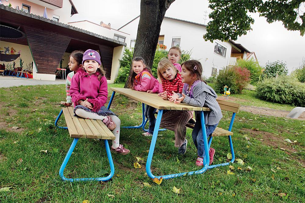 Ruhepausen für Kinder – Sechs Mädchen sitzen im Garten an einer Kindersitzgruppe aus Holz.