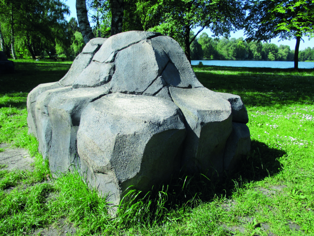Spielplatzgestaltung – Eine dekorative Sitz- und Klettermöglichkeit in Form eines grauen Felsens.