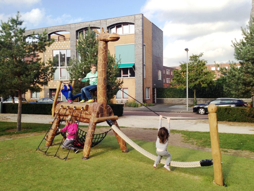 Spielplatzgestaltung – Ein Klettergerät in Form einer Giraffe, auf der vier Kinder herumklettern.