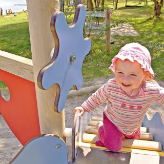 Wahrnehmung fördern – Ein kleines Mädchen klettert auf eine bunte Spielanlage für Kleinkinder.