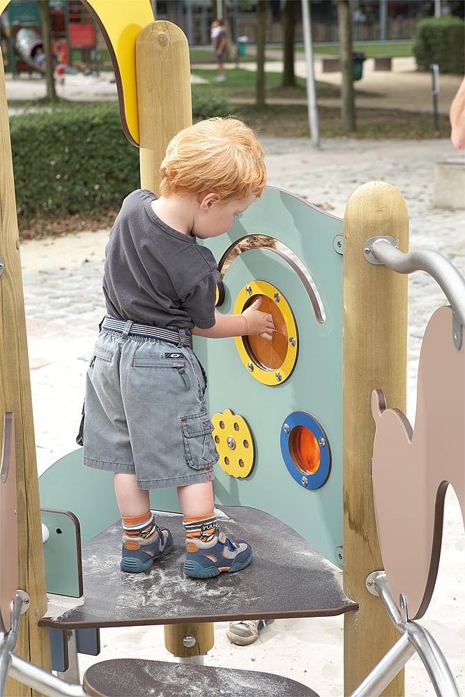 Wahrnehmung fördern – Ein kleiner Junge steht auf einer Spielanlage und betastet integrierte Spielelemente.