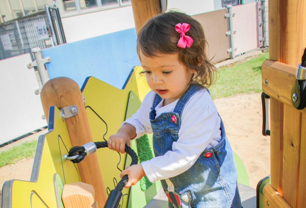 Wahrnehmung fördern – Ein kleines Mädchen zieht an einer Schlinge aus Tau, die an einer Spielanlage befestigt ist.